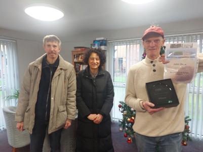 A picture of John Shaw being presented with his trophy and certificate for winning the Best Community Garden prize